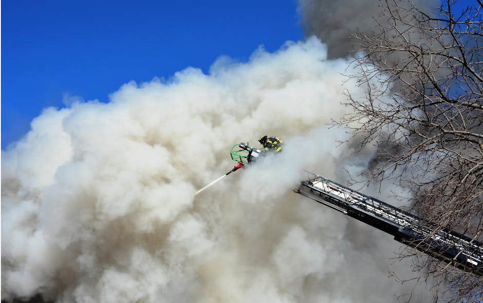 Firefighters on aerial ladder directing water stream into smoke