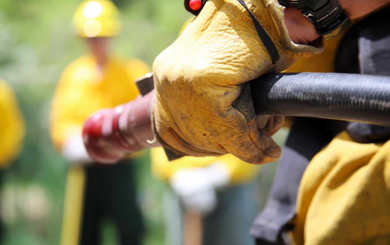 Wildland firefighter close-up with yellow Nomex turnout sleeve and hose nozzle