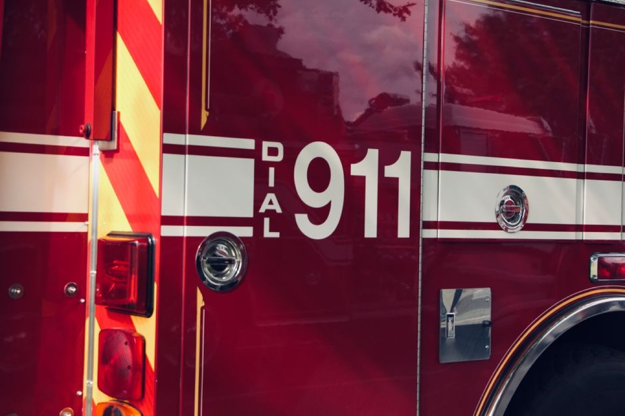 Close-up of the side of a modern American red fire engine with white DIAL 911 lettering and chevron striping