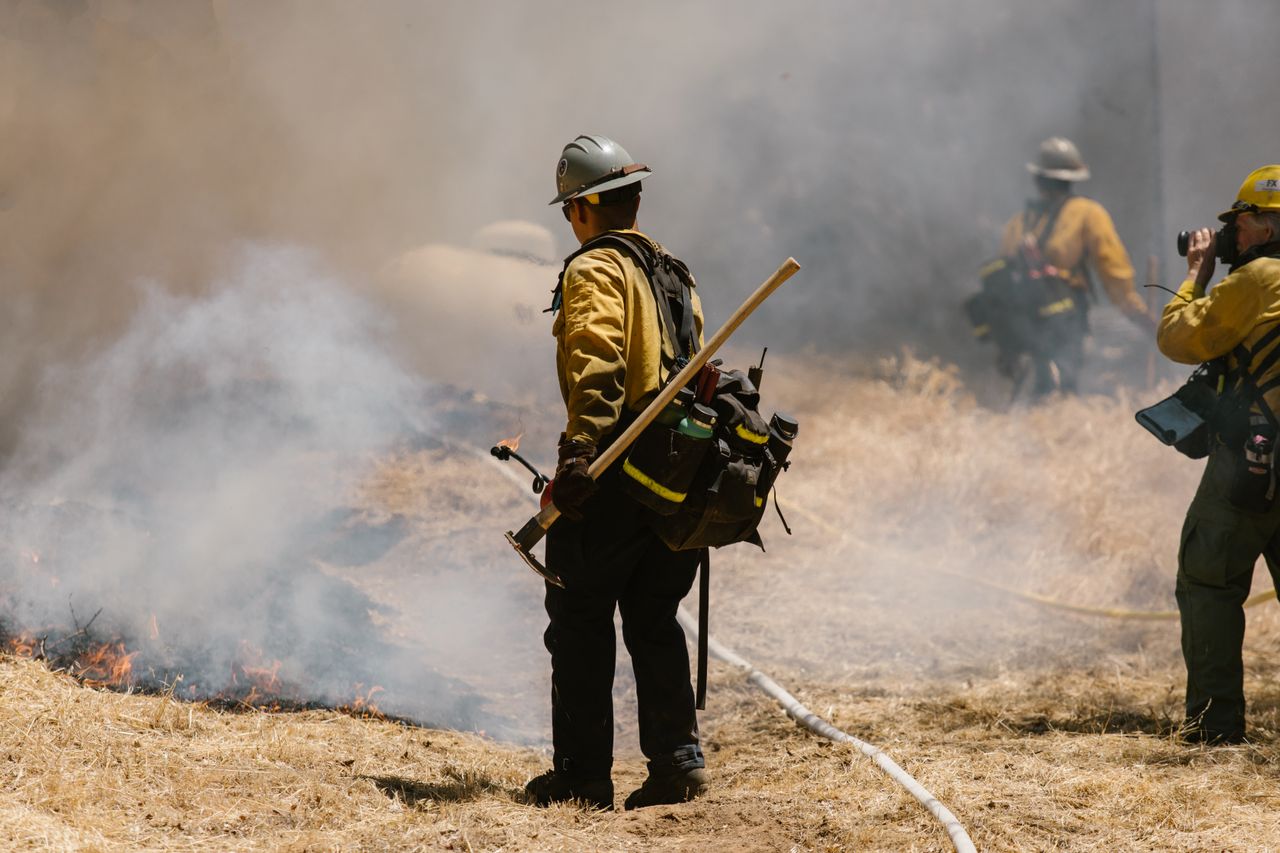 Wildland firefighter in gear battling a forest fire with smoke and flames visible