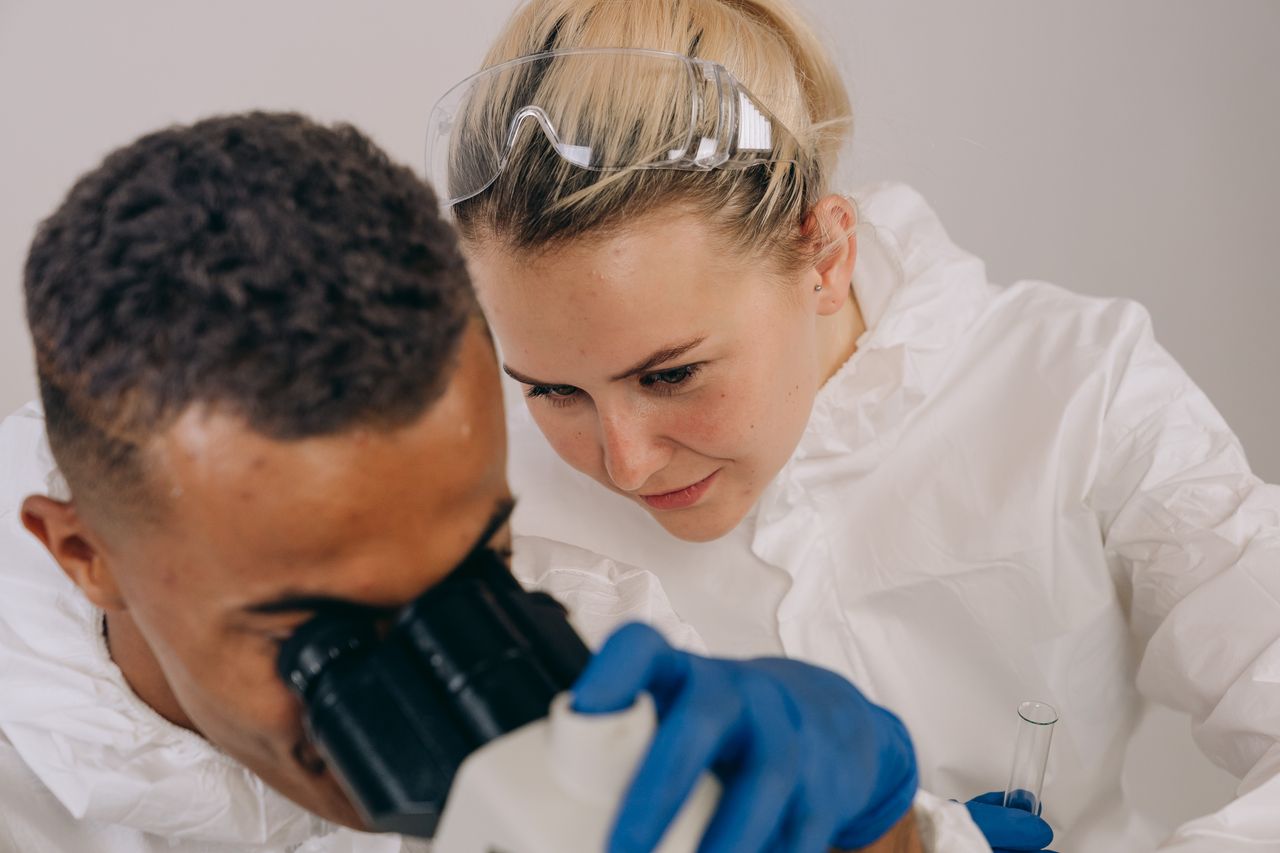 Two scientists in lab gear engaged in collaborative microscopic research