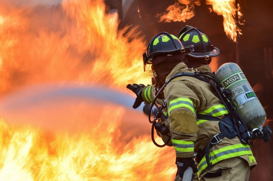 Two firefighters in full turnout gear and SCBA directing a hose at an active fire