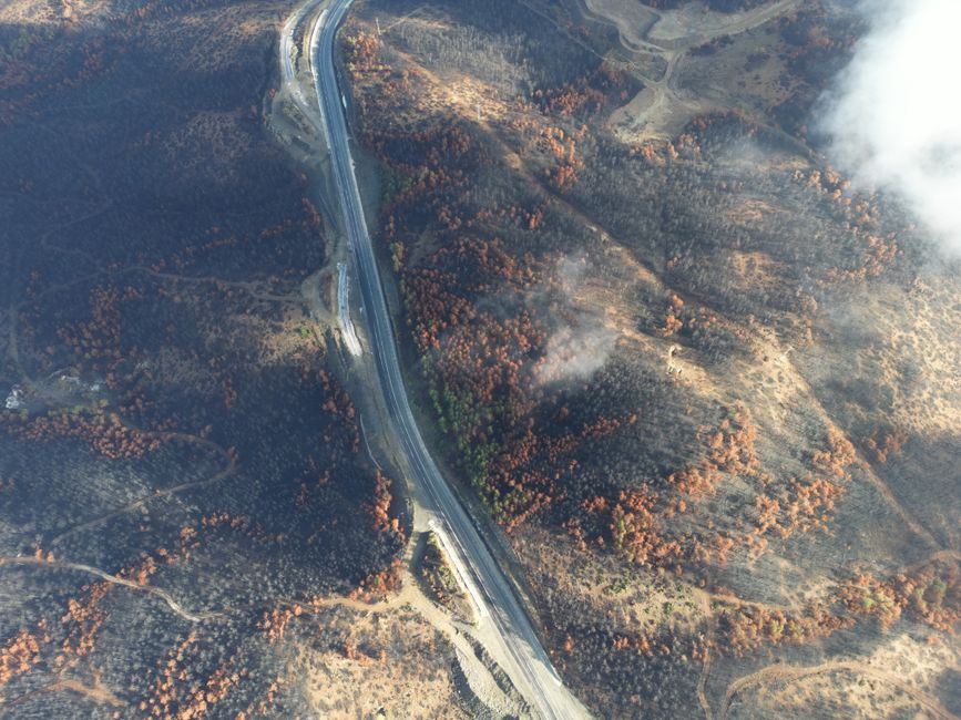Aerial view of a wildfire-affected landscape with smoke rising from scorched terrain