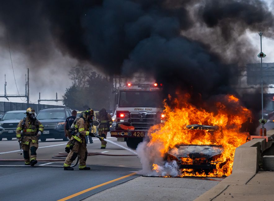 American firefighters directing hose streams onto a fully involved vehicle fire on a roadway