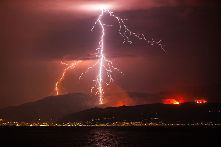 Lightning bolt striking near forest landscape at night