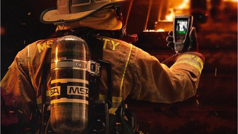 Firefighter wearing an MSA G1 SCBA with American-style helmet checking a handheld display near an active fire
